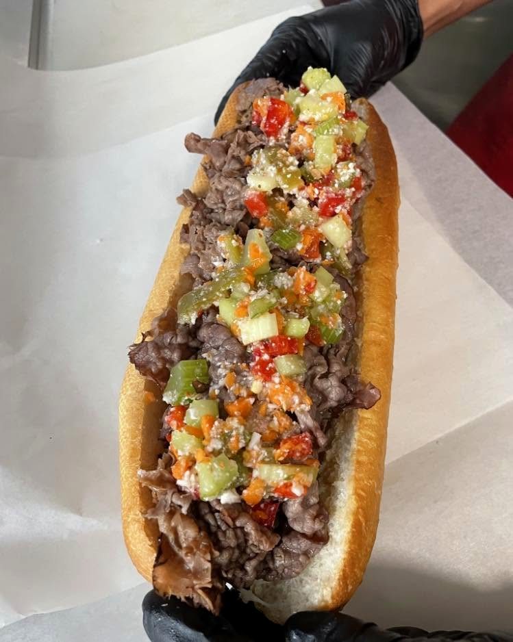 A gloved hand holding an Italian beef piled with giardiniera